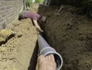 Plumber installing a new sewer pipe in an excavated trench beside a Galveston home